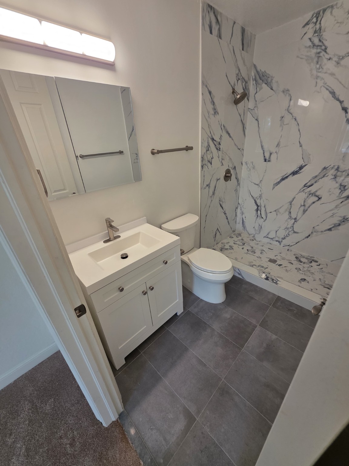 Completed bathroom with white vanity, gray tile floor, and marble-look shower walls